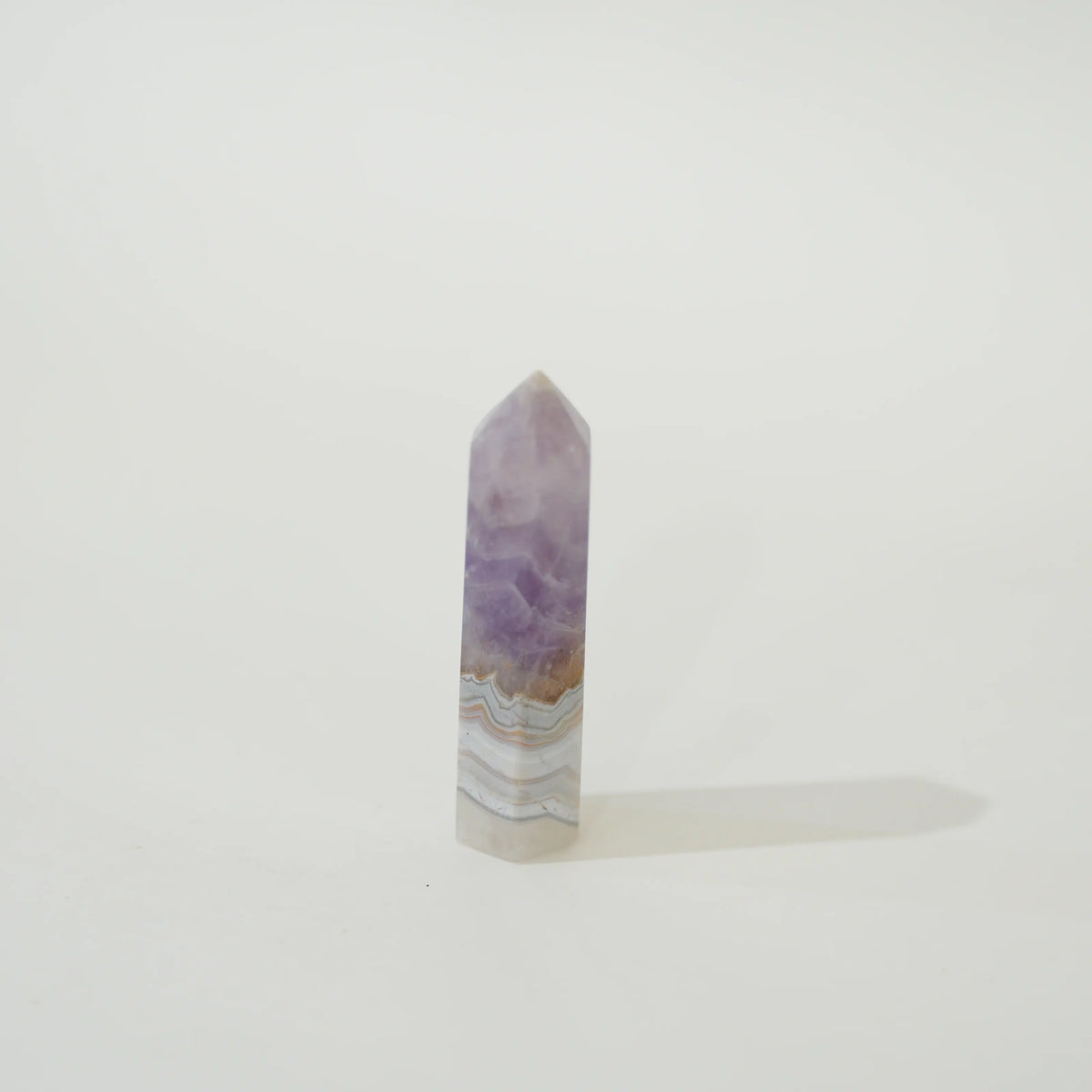 A polished Amethyst & Mexican Lace Agate Tower with natural banding of purple, white, and light brown, standing upright on a white surface against a white background.