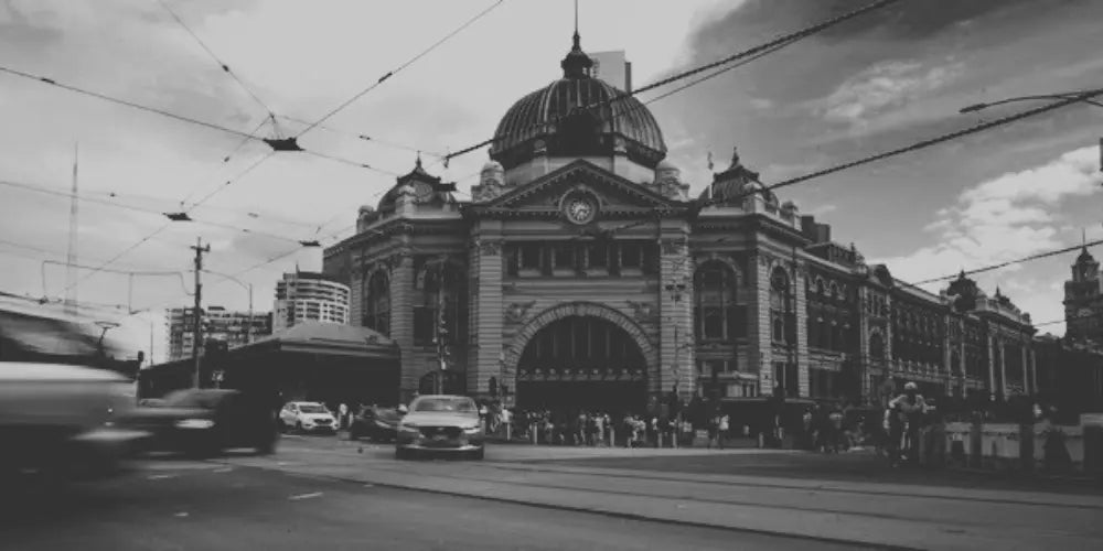 Black and white image of a Flinders station at melbourne , with cars and trams on the street.