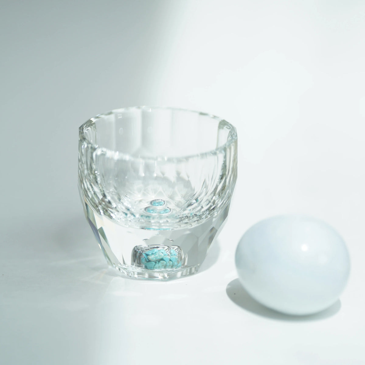 Close-up of a clear Crystal Turquoise Faceted Cup on a white surface, casting soft shadows.