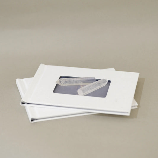 Two white square frames stacked on a neutral beige background, each with a small clear rectangular window showing a gray rectangular item inside.