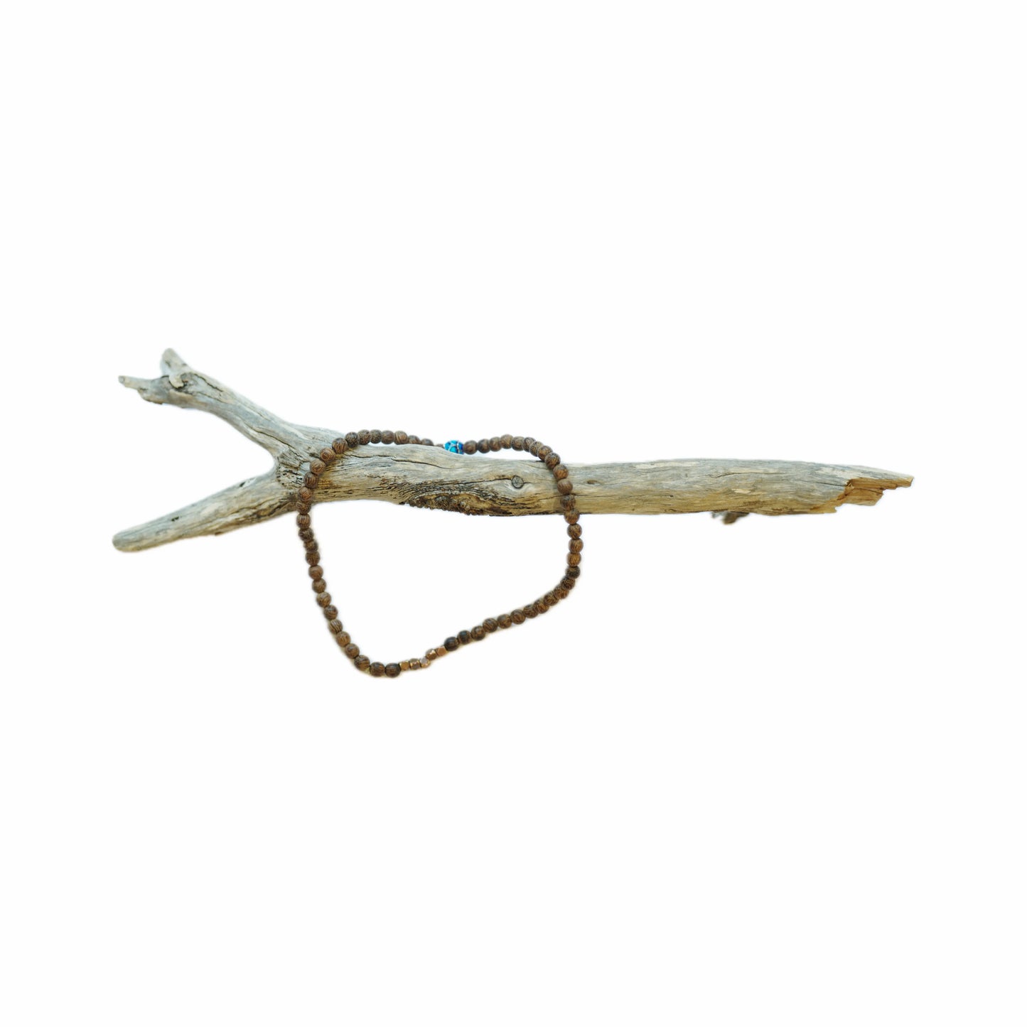 A rustic wooden branch showcasing a simple, earthy bead necklace, featuring brown and blue beads, artistically draped over it.