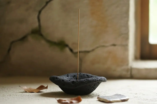 Incense stick in a black ceramic holder on a stone surface with a blurred background