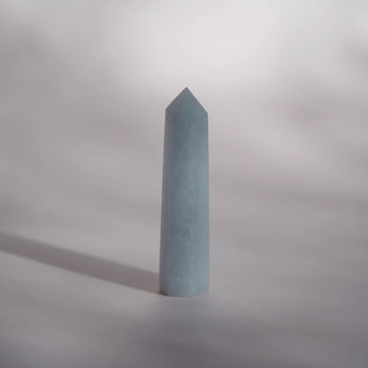 A celestite crystal tower or obelisk standing upright on a neutral gray surface with a soft shadow cast to the left.