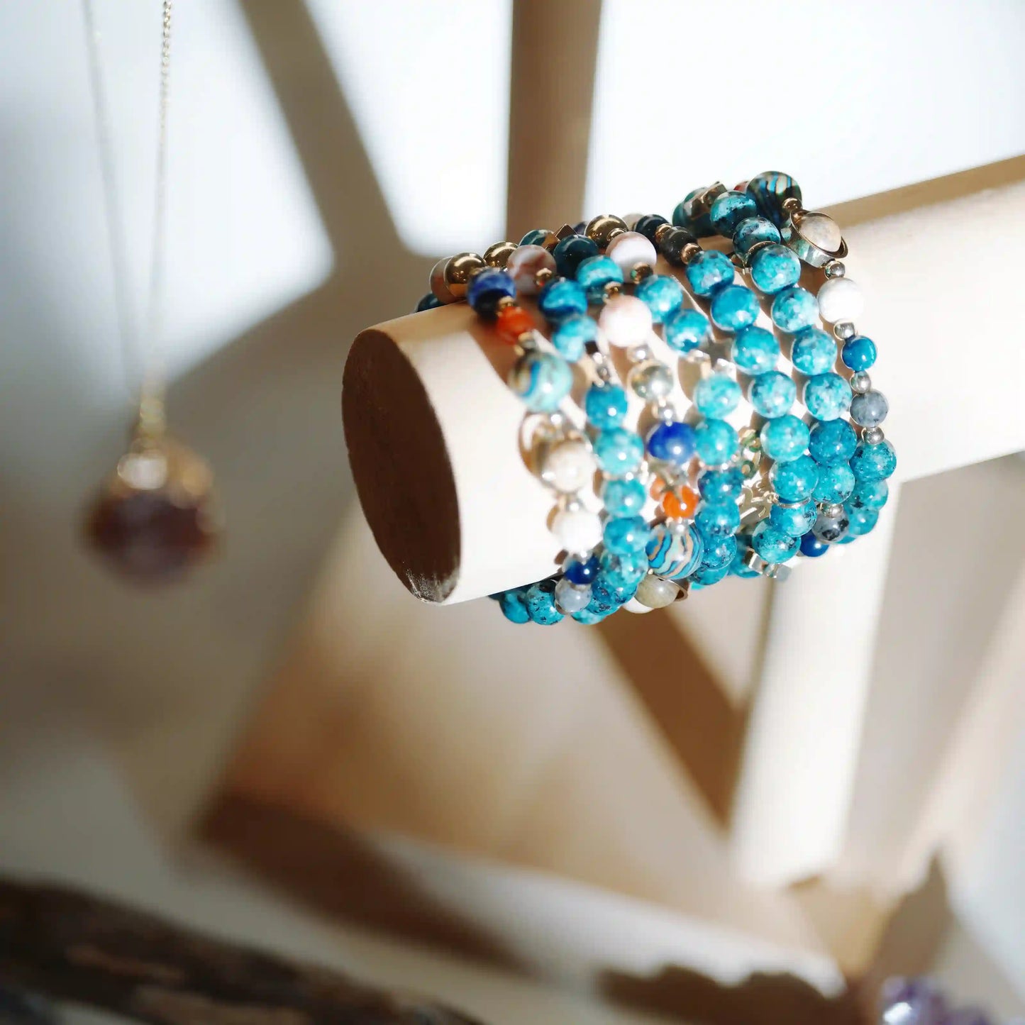 Blue Constellation Crystal bracelets with turquoise, blue, white, and orange beads displayed on a light wood cylindrical stand.