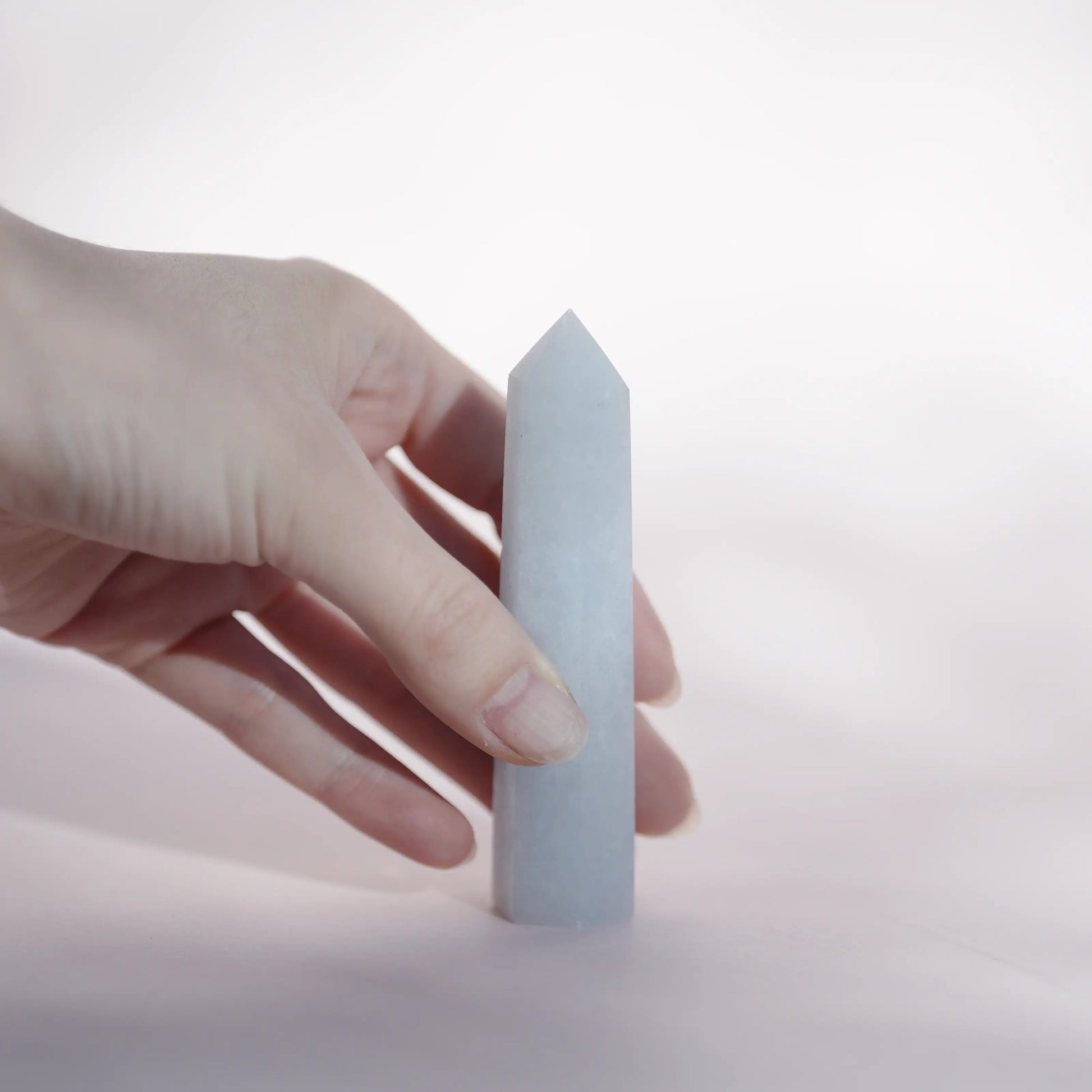 A hand holding a celestite tower  against a soft white background.