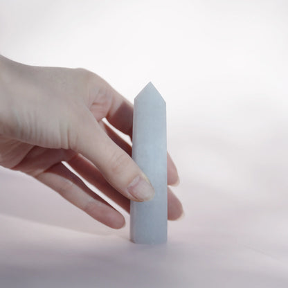 A hand holding a celestite tower  against a soft white background.