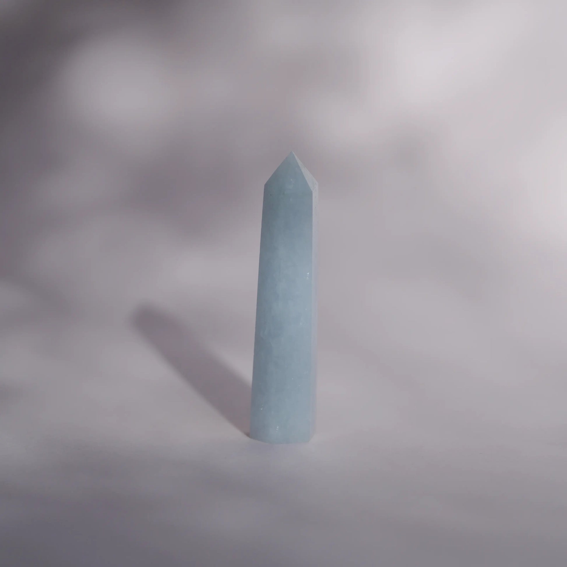 A pale blue celestite tower standing upright on a soft gray surface with a soft shadow cast to the left.