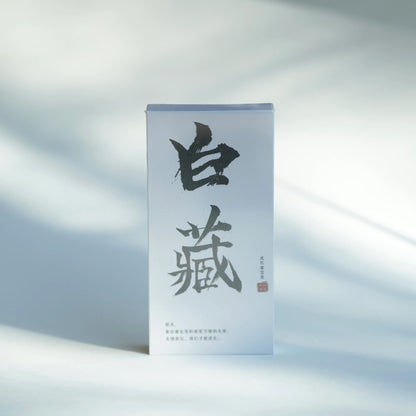 A tall, narrow white product box with large black Chinese calligraphy and small red seal details, standing upright on a softly lit white surface with natural shadows.