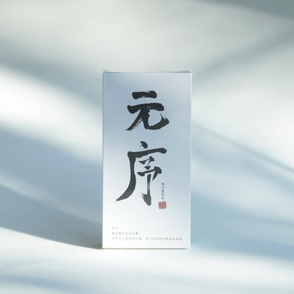 A tall, narrow white product box with large black Chinese calligraphy on the front and a small red seal, standing upright on a softly lit white surface with dappled shadows.