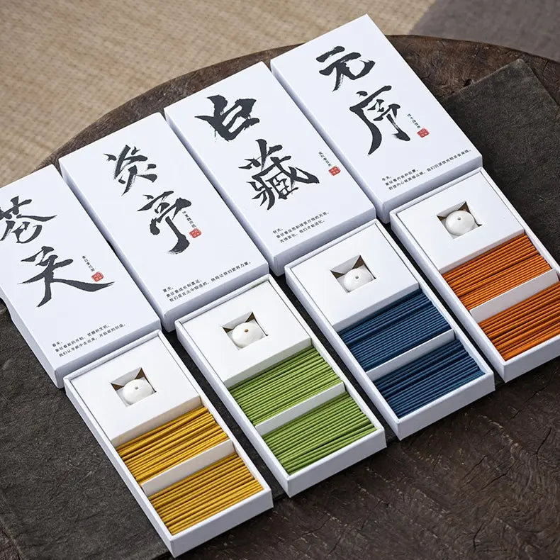 Six white rectangular boxes with large black Chinese calligraphy characters are arranged on a dark wooden surface, each open to reveal a stack of thin colored cords or ribbons in yellow, green, blue, and orange. The boxes also contain small white circular items.