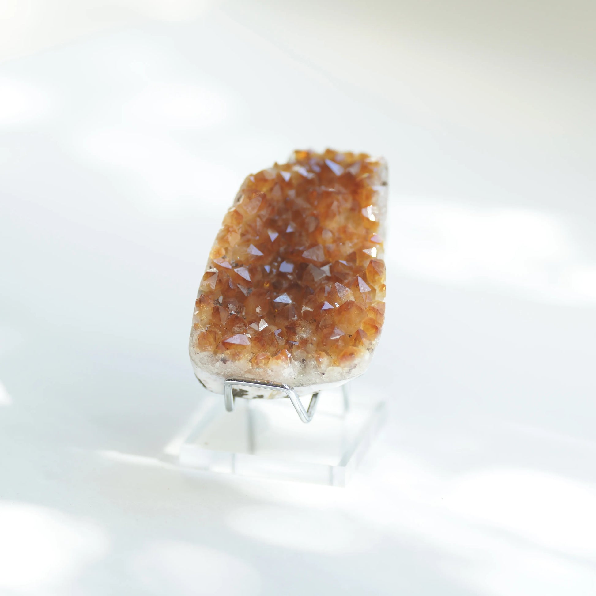 A citrine crystal cluster with brown and amber-colored crystalline points, mounted on a clear acrylic stand against a bright white background.