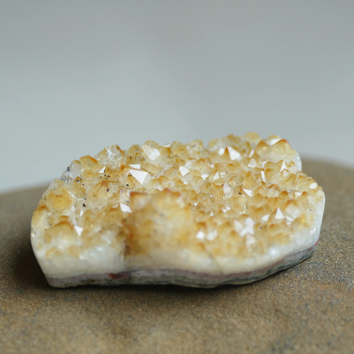 A natural crystal cluster specimen with pale yellow and cream quartz points on a rough white and gray base, photographed on a neutral gray background.