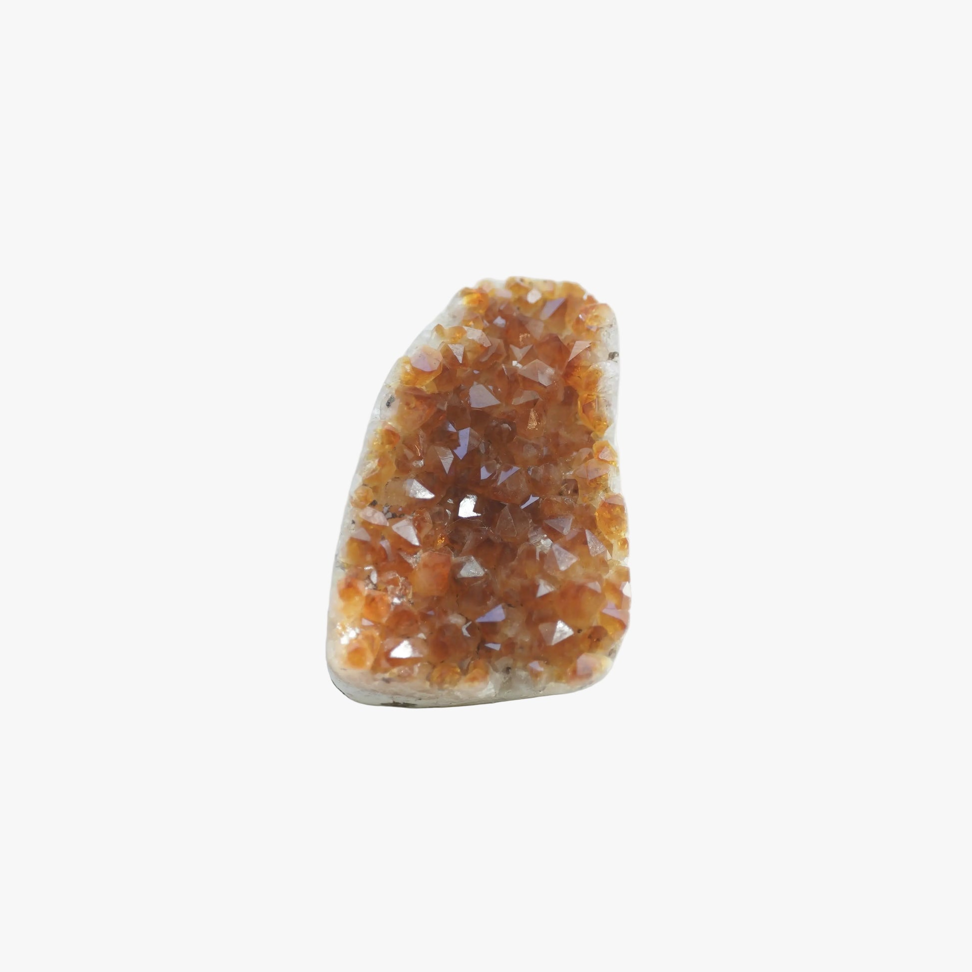 A raw crystal cluster geode with orange-brown crystalline points on a light beige matrix, photographed on a white surface with soft leaf shadows.