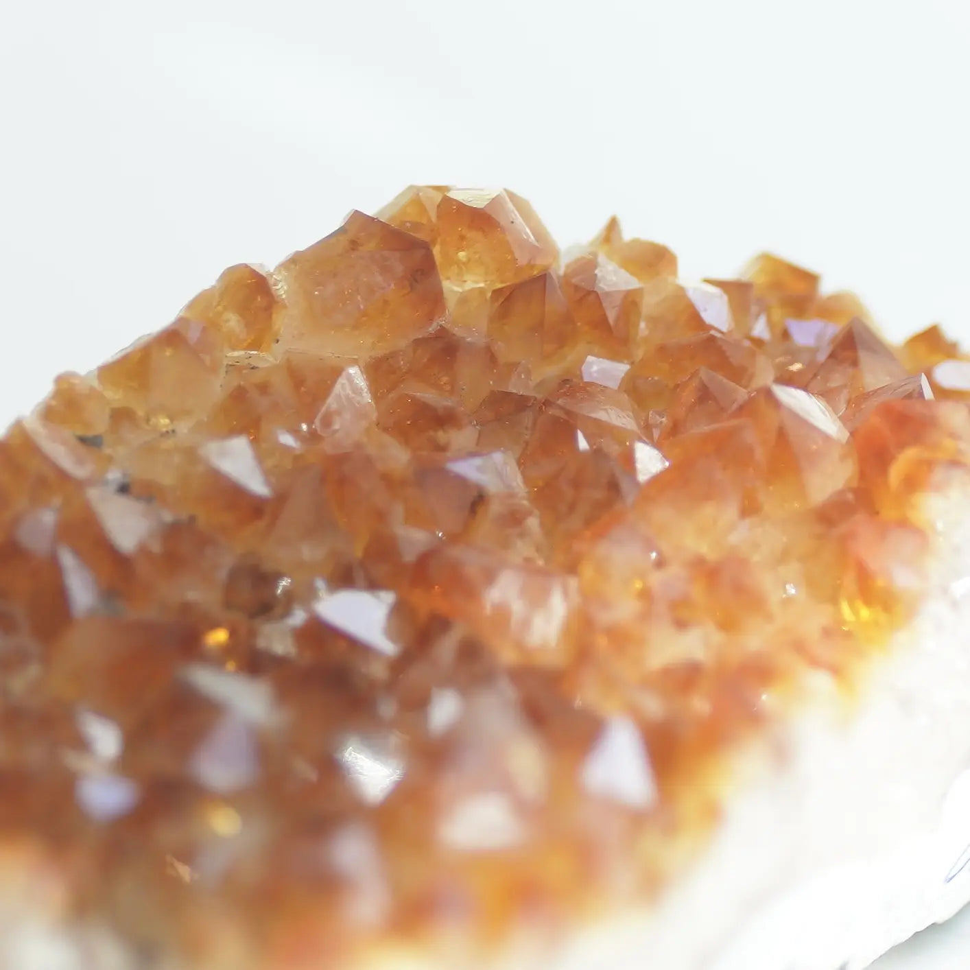 A close-up of a natural crystal cluster with faceted orange-brown translucent stones on a white base, photographed against a bright white background.