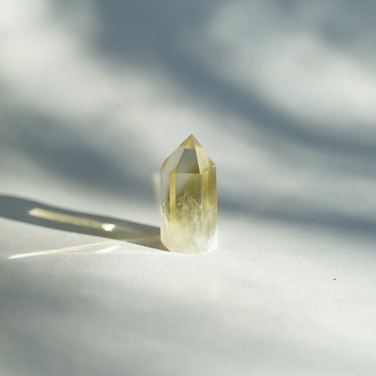 A natural yellow citrine crystal point tumbler standing upright on a light surface, captured in bright sunlight with soft shadows.