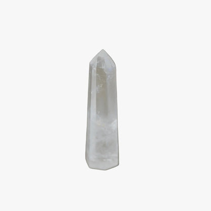 A natural clear quartz crystal point tower standing upright on a neutral gray surface with a soft shadow cast to the right.