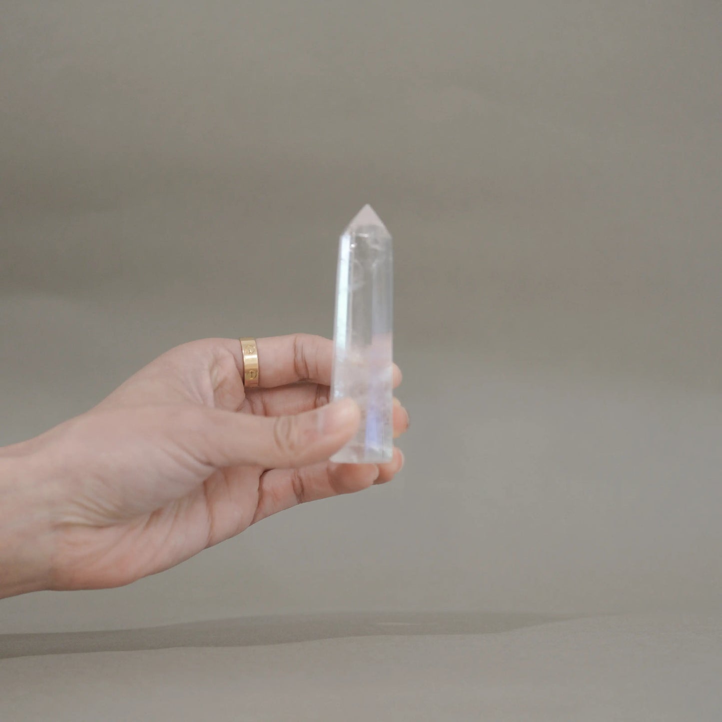 A hand holding a clear quartz crystal point against a neutral gray background.