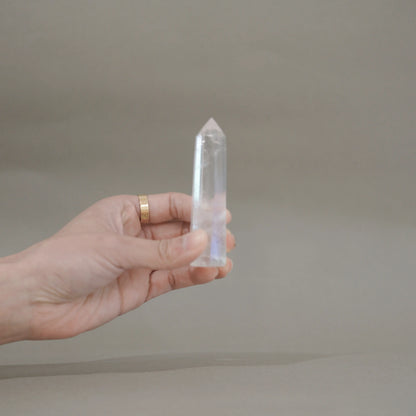 A hand holding a clear quartz crystal point against a neutral gray background.