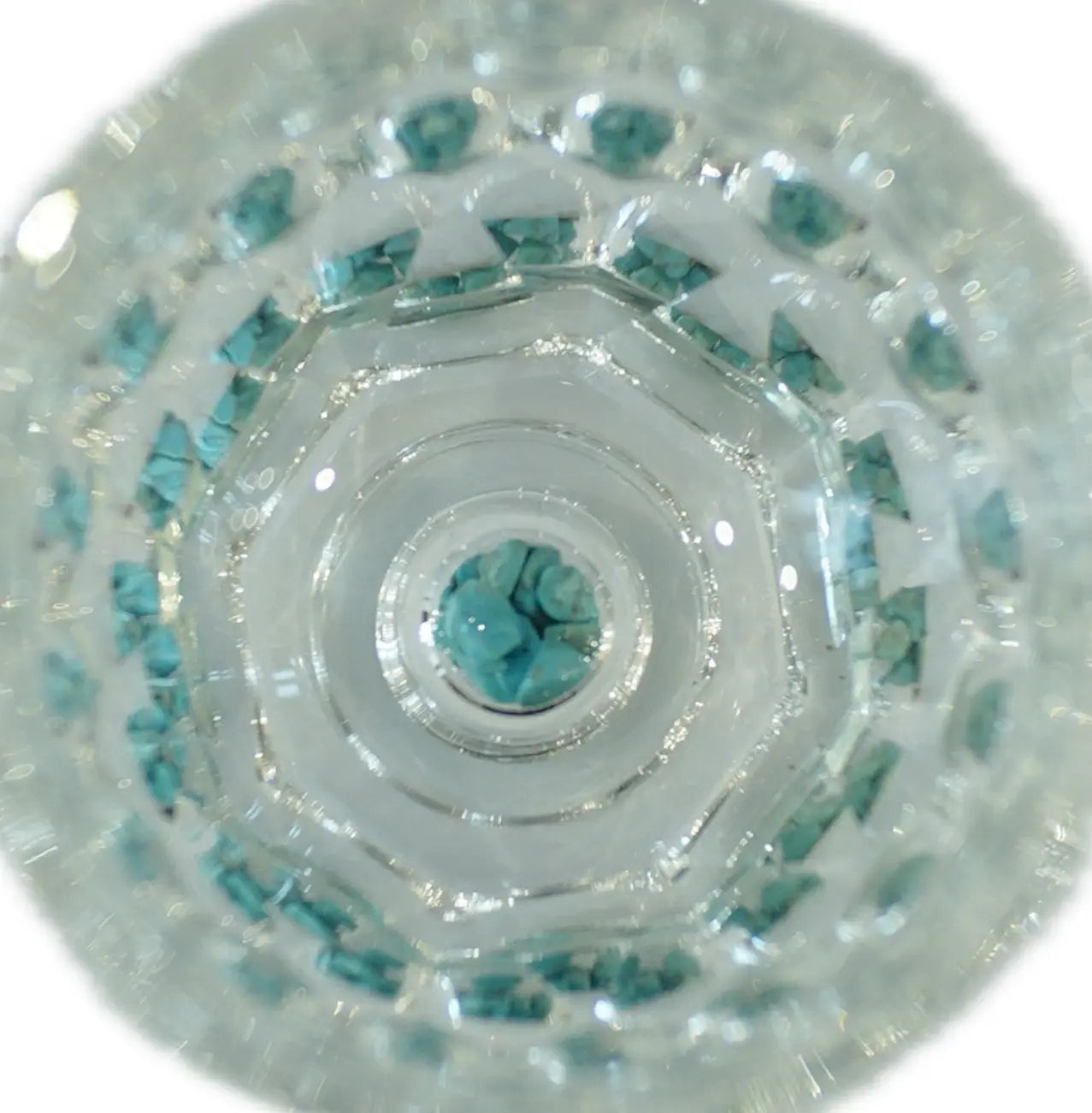 Close-up view of a crystal cup filled with turquoise stones, showcasing intricate layering and light refraction.