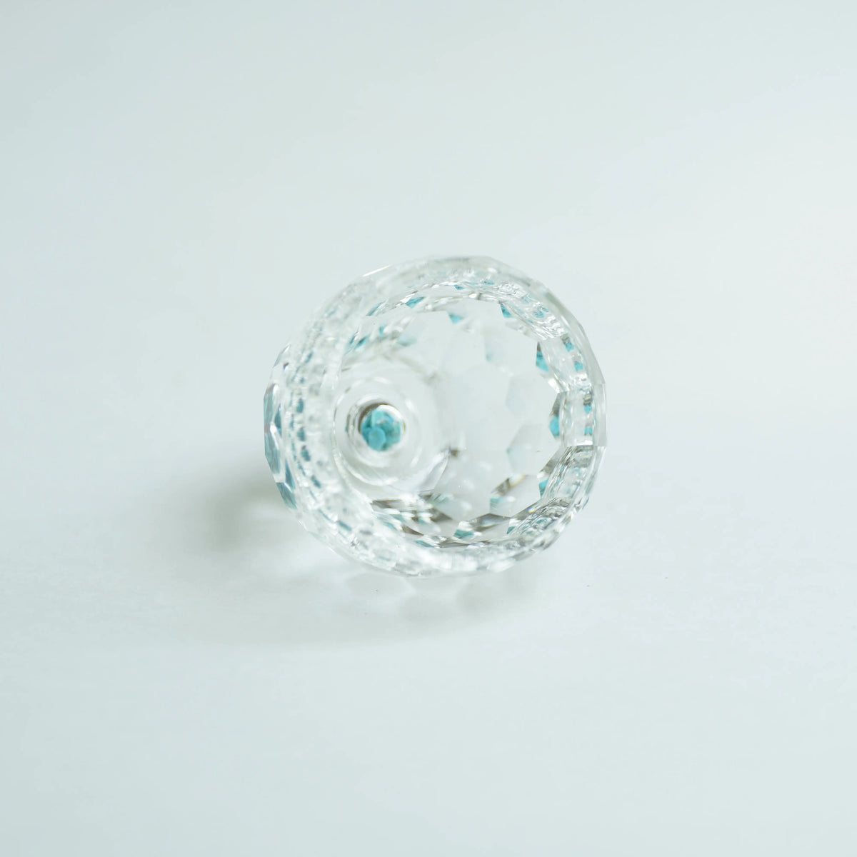 Close-up of a faceted clear tea cup with blue reflections on a pale background.