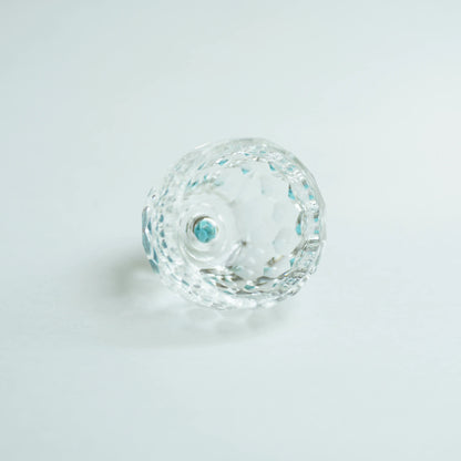 Close-up of a faceted clear tea cup with blue reflections on a pale background.
