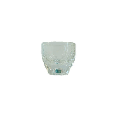 Clear glass tumbler with a curved design and decorative patterns around the rim, resting on a plain background.