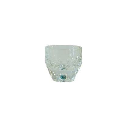 Clear glass tumbler with a curved design and decorative patterns around the rim, resting on a plain background.