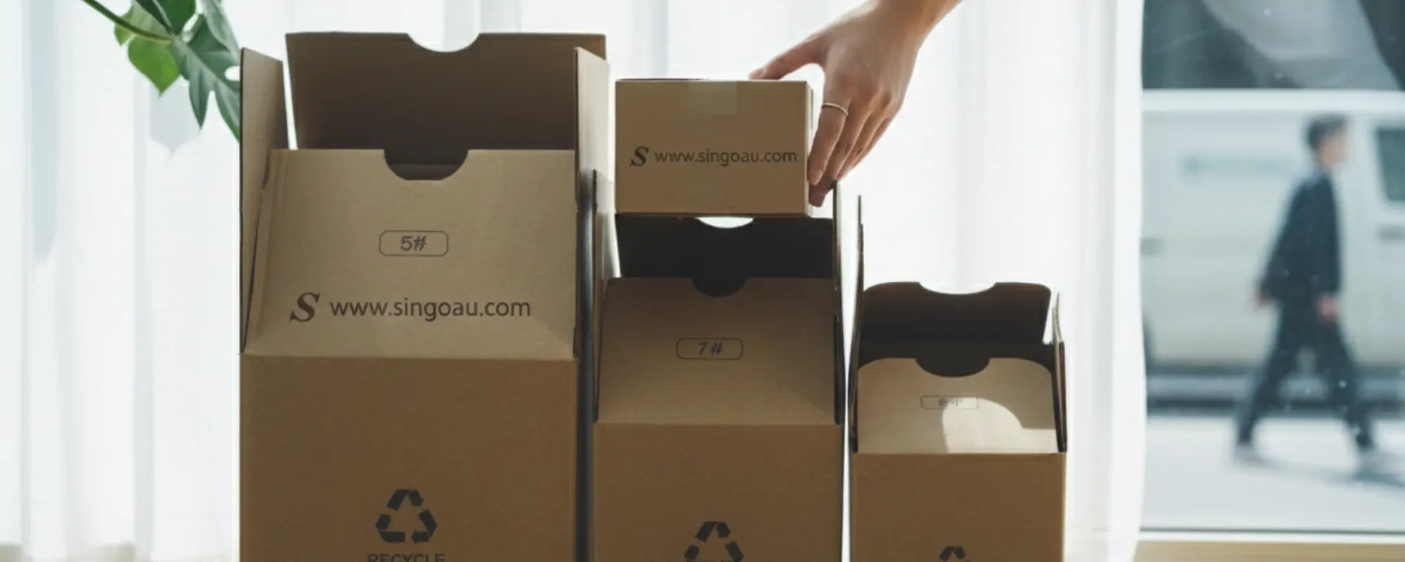 Person opening a cardboard box with 'Singo' branding in a bright room.