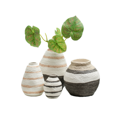 Four decorative vases in light neutral tones, featuring striped patterns and lush green leaves in the tallest vase.