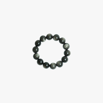 Handcrafted 18mm Silver Sheen Obsidian crystal bracelet with mesmerizing natural chatoyancy, viewed top-down on a clean white background for grounding and reflection at Singoau