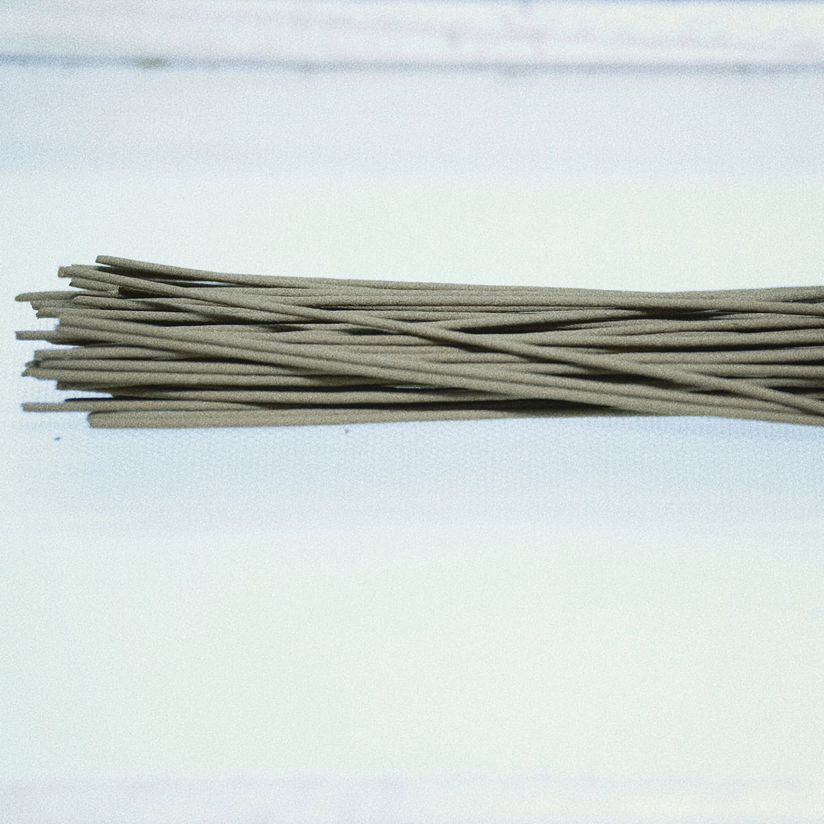 A bundle of thin, light brown wooden incense sticks or rods arranged horizontally on a plain white surface.