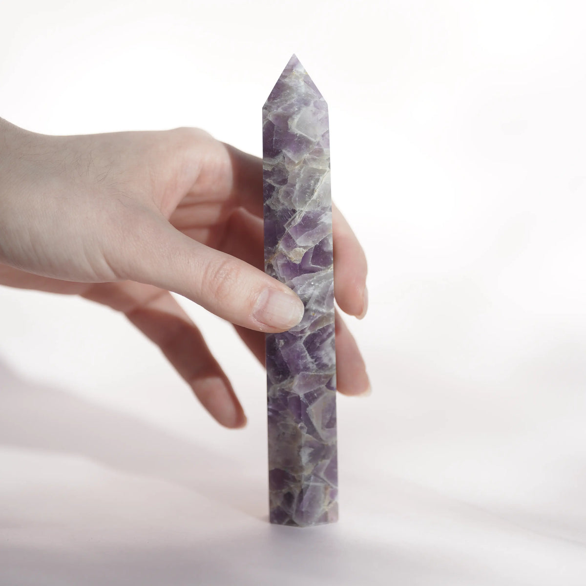 Hand holding a polished purple-and-white fluorite crystal tower against a white background.