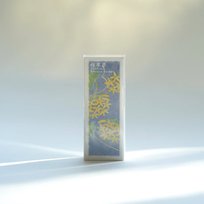 Kousaido Ikadenshin Japanese Incense Telosma cordata scent on a white surface, wrapped in clear plastic. The cover is blue with yellow floral illustrations and small white Japanese text near the top.