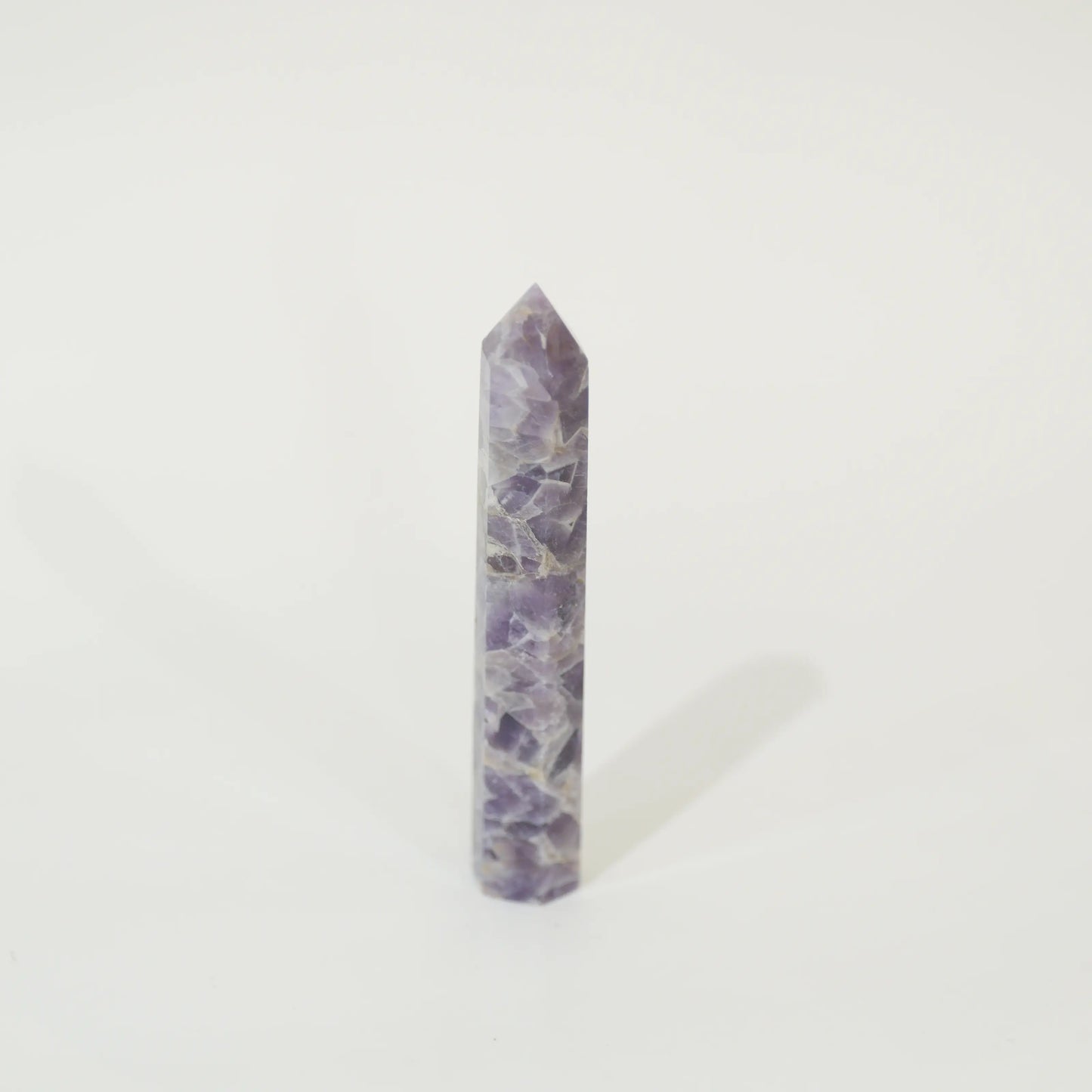 A polished purple amethyst crystal point tower standing upright on a clean white background.