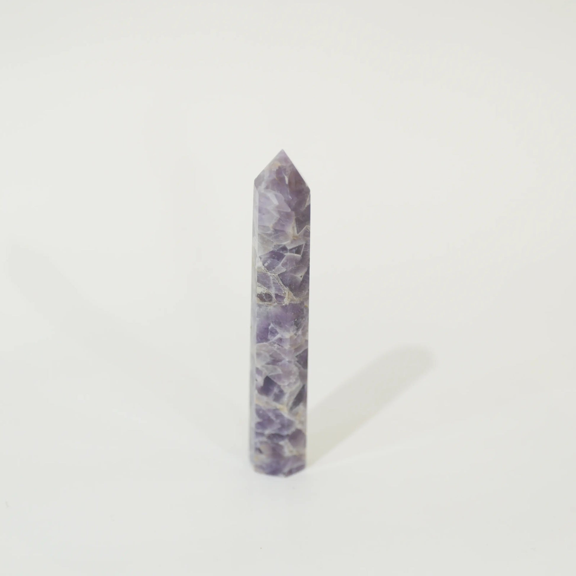 A polished purple amethyst crystal point tower standing upright on a clean white background.