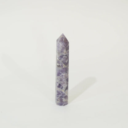 A polished purple amethyst crystal point tower standing upright on a clean white background.