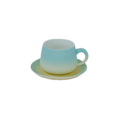 A small ceramic cup and saucer set with a smooth ombre gradient transitioning from light blue at the top to off-white at the bottom, set against a plain white background.