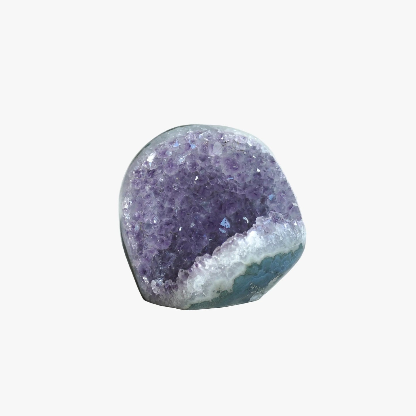 A polished amethyst geode specimen with a purple crystal interior and a white to blue crystalline outer base, photographed on a softly lit white fabric surface.