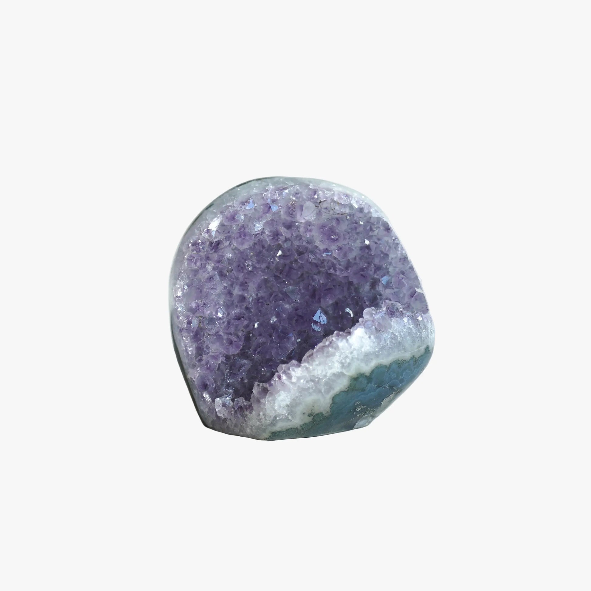 A polished amethyst geode specimen with a purple crystal interior and a white to blue crystalline outer base, photographed on a softly lit white fabric surface.