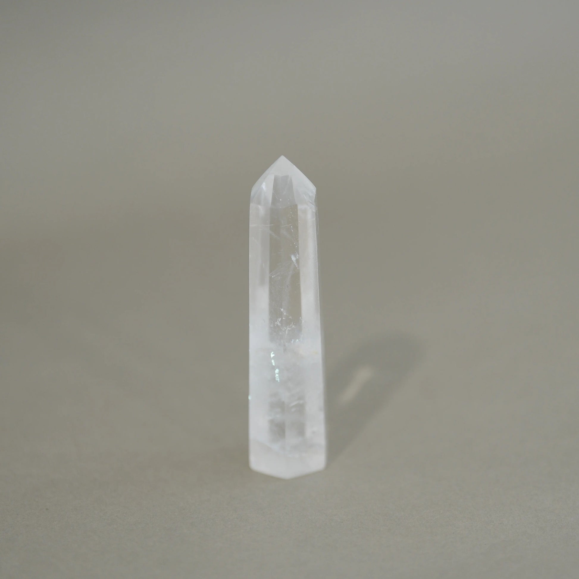 A natural clear quartz crystal point tower standing upright on a neutral gray surface with a soft shadow cast to the right.