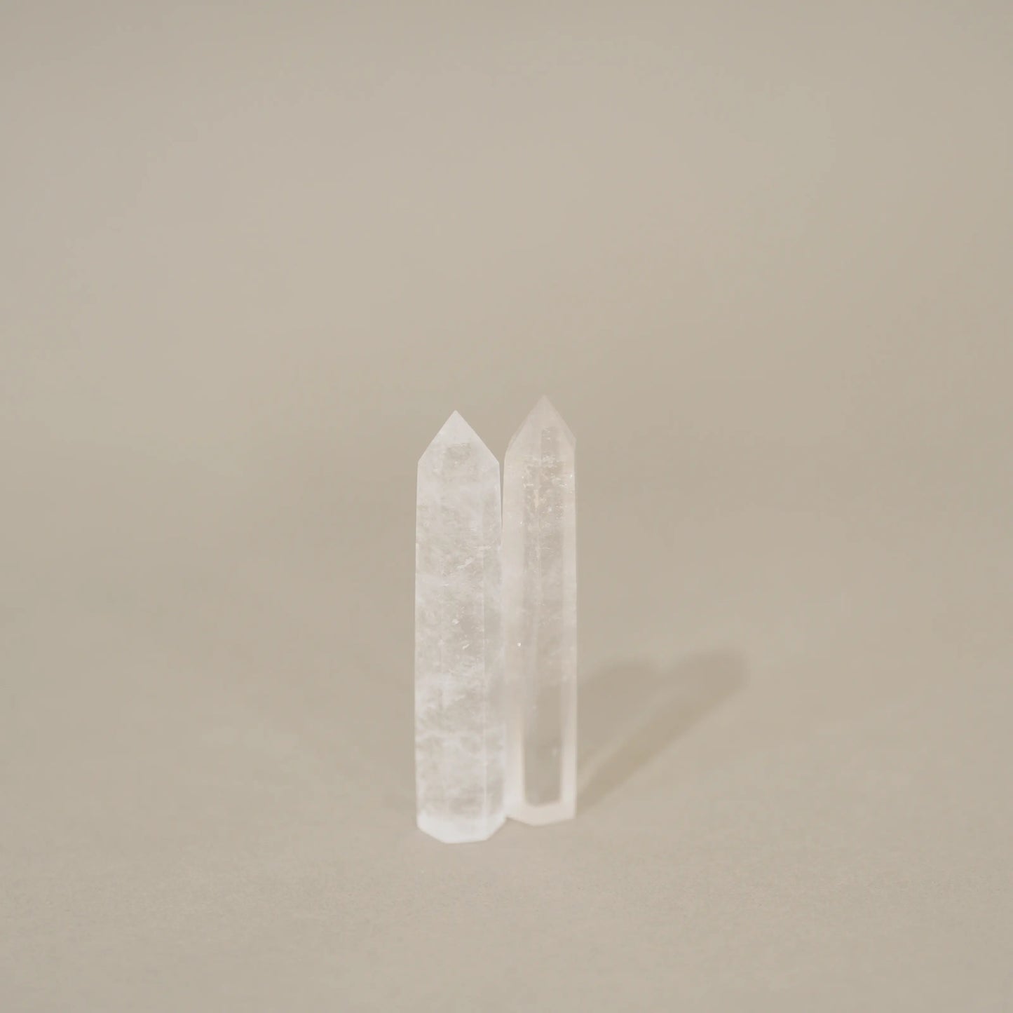 Two clear crystal point towers standing upright on a neutral beige background.