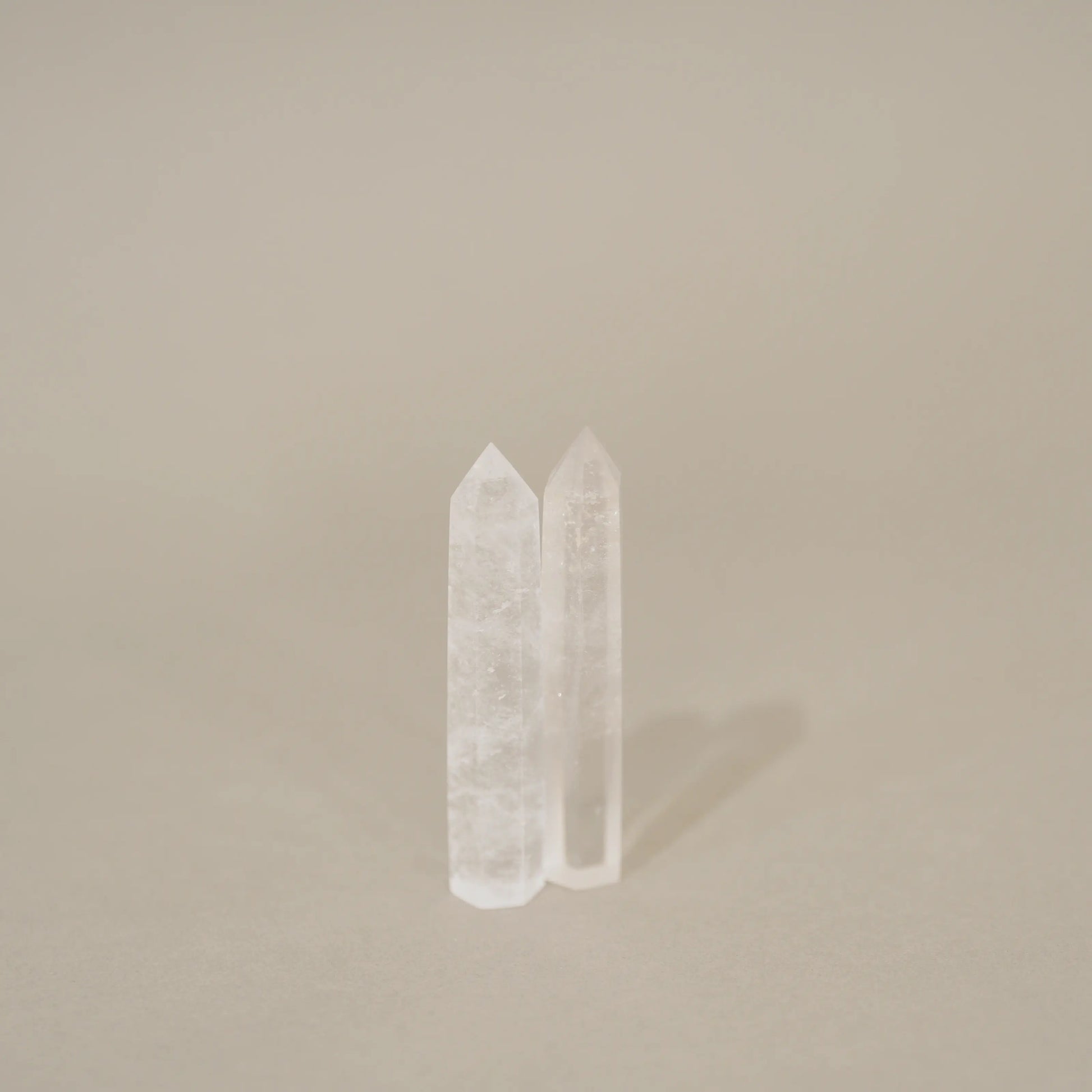 Two clear crystal point towers standing upright on a neutral beige background.