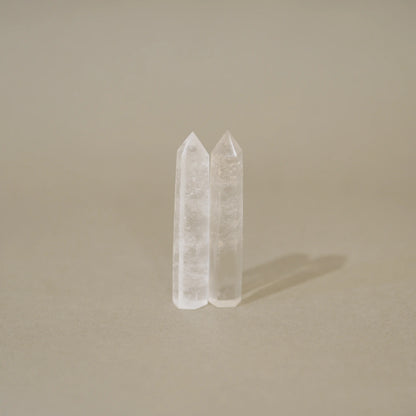 Two clear quartz crystal points standing upright on a neutral beige surface against a matching beige background.