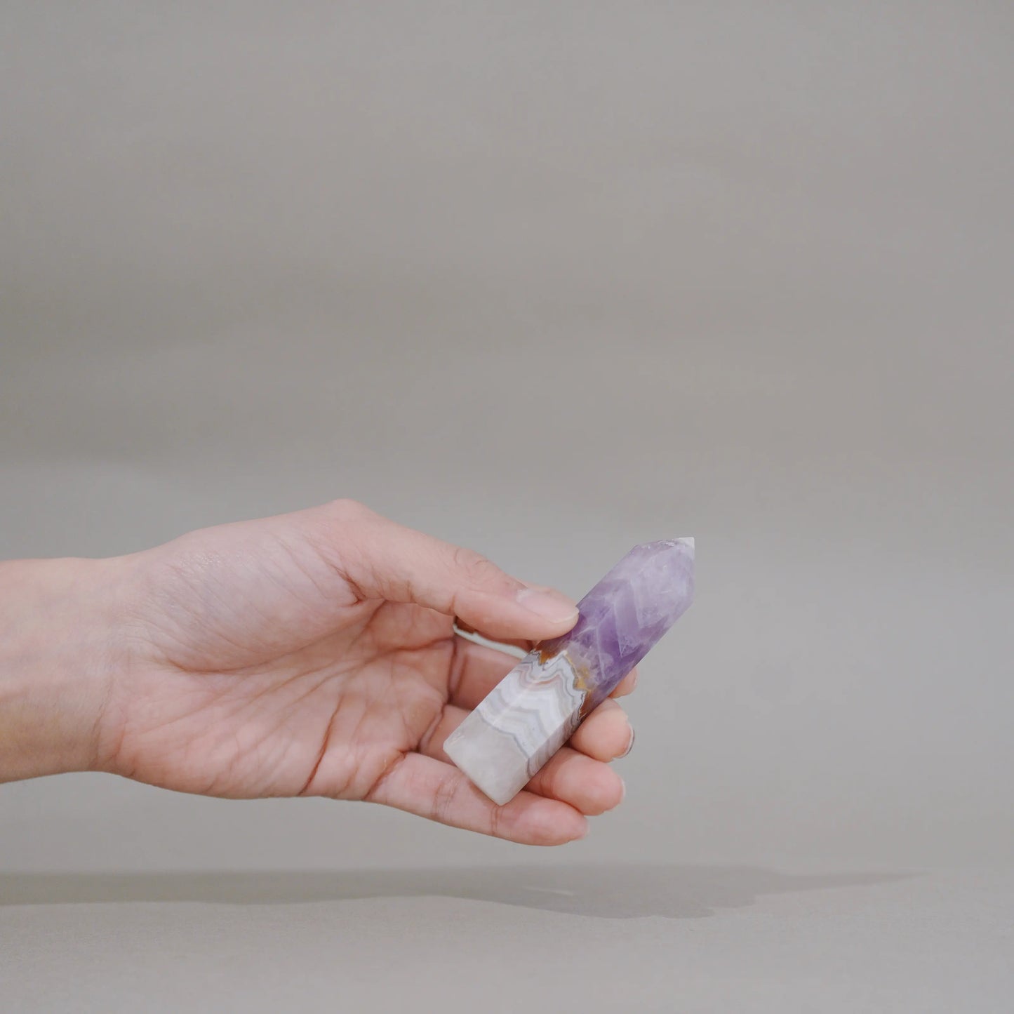 A hand holding a small polished crystal point with a white base and a purple top, photographed against a plain light gray background.
