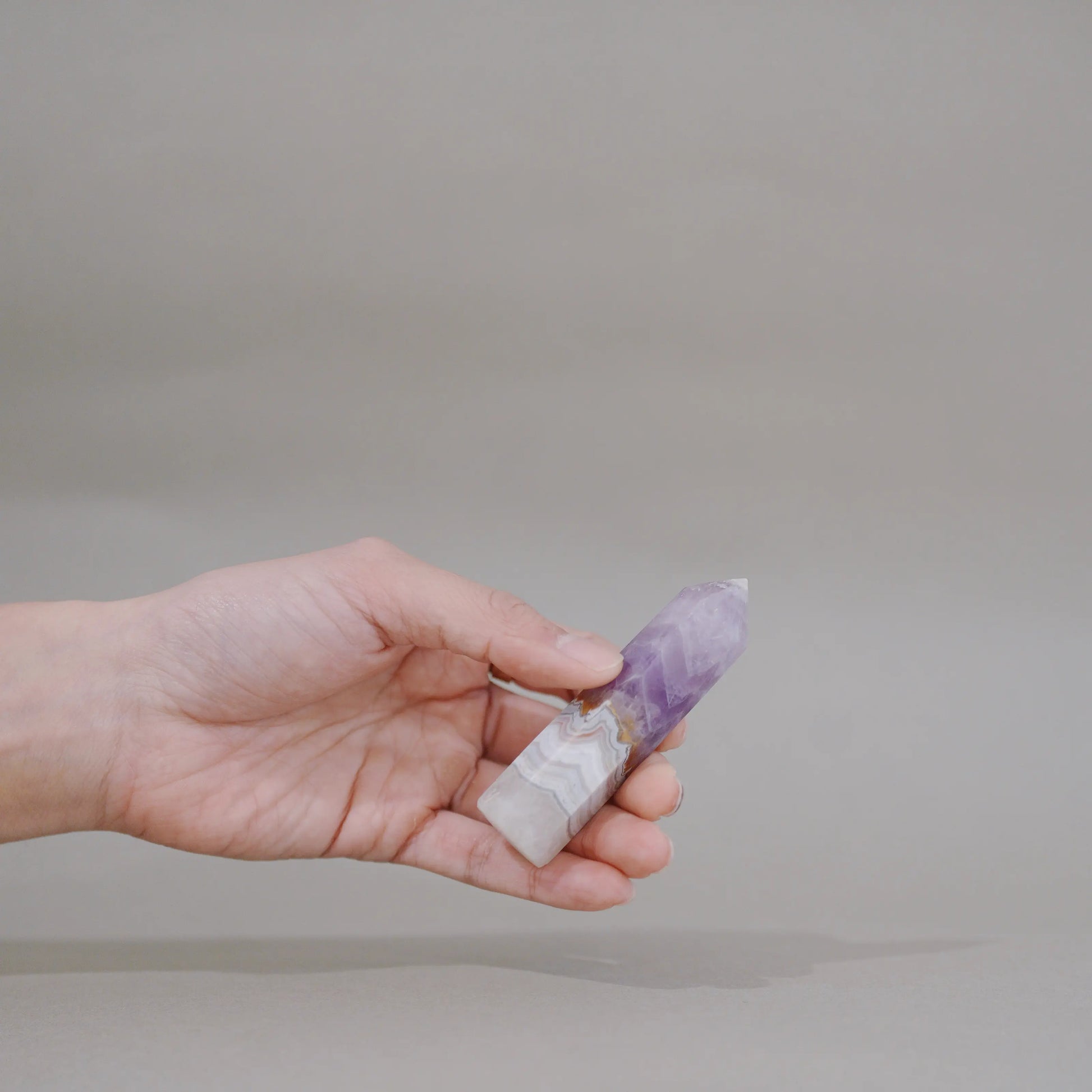 A hand holding a small polished crystal point with a white base and a purple top, photographed against a plain light gray background.