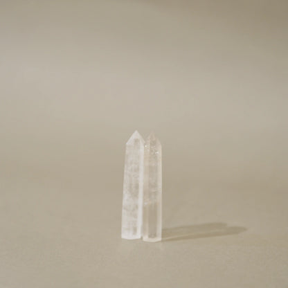Two clear pointed crystal towers standing upright on a warm beige surface against a matching beige background.