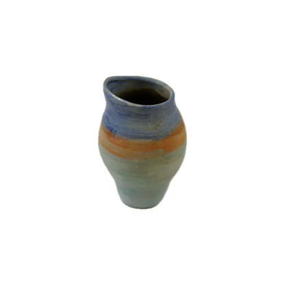 A handcrafted ceramic jug with textured stripes of blue, orange, and pale green, featuring a curved lip and a rounded body on a white background.