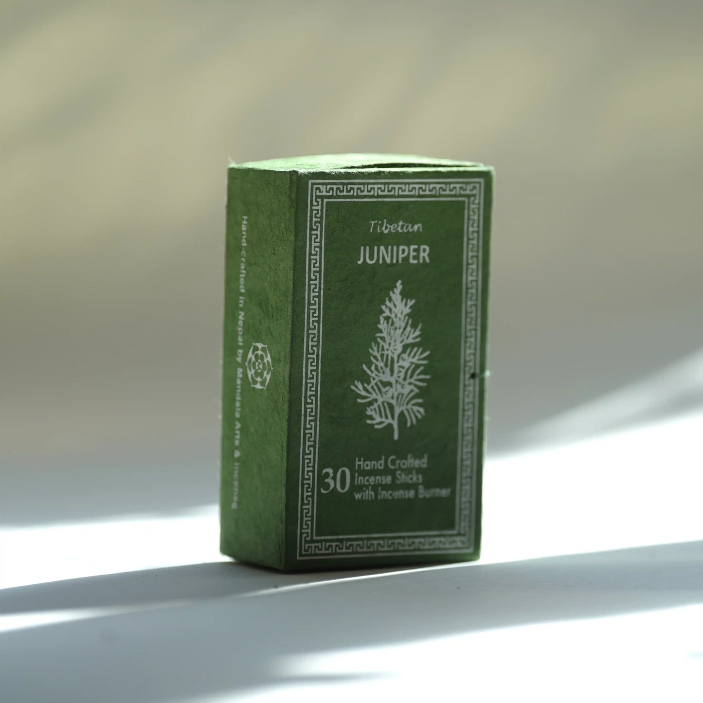 A green rectangular box of Tibetan Juniper handcrafted incense sticks with a white printed tree illustration and text, photographed on a light surface with soft shadows.