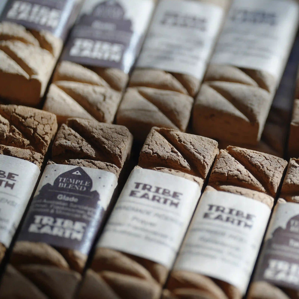 Close-up of packaged artisanal flatbread loaves from Tribe Earth, with white paper labels wrapped around the loaves and a warm brown background.