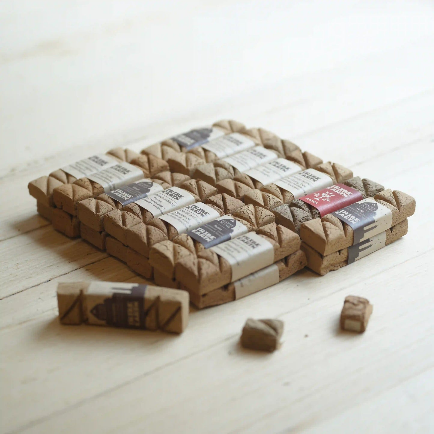 A set of tribe earth incense with wrapped paper labels, arranged on a light wood surface with a few loose stamps in front.